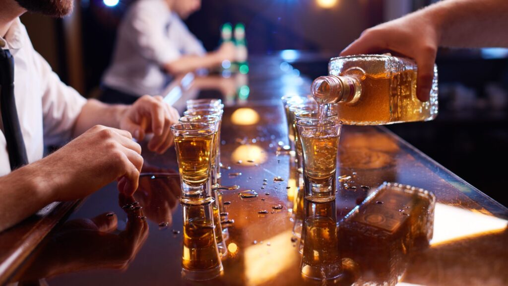a person pouring a drink into shot glasses