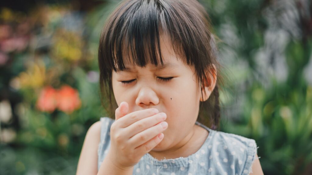 a girl with her eyes closed and her hand over her mouth coughing