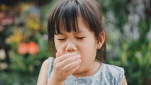 a girl with her eyes closed and her hand over her mouth coughing